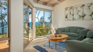 A modern living room with a green sofa, a wooden coffee table, and a view of the sea through large sliding glass doors. - Windarra on Denhams Unit Two (DENHAMS BEACH)