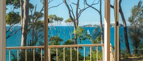 A coastal view from a balcony with trees and a clear blue sea.