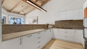 Une cuisine moderne avec des meubles blancs, un plan de travail en bois et une grande fenêtre.