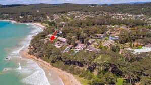 An aerial view of a coastal residential area with houses, a beach, and dense greenery. - Windarra on Denhams Unit Two (DENHAMS BEACH)