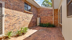 A brick building with a small patio area, a window, and a door with a metal grille.