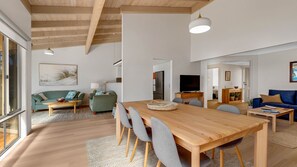 A modern living space with a dining area, sofas, a TV, and a kitchen in the background. - Windarra on Denhams Unit Two (DENHAMS BEACH)