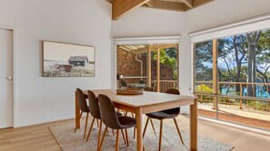 Un coin repas avec une table et des chaises en bois, une vue sur un mur de briques et une grande fenêtre donnant sur un paysage naturel.