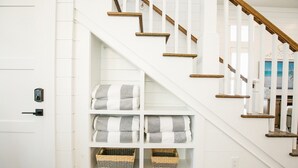Un escalier avec des marches en bois et des rampes blanches, menant à un palier où se trouvent des étagères remplies de serviettes pliées et de paniers.