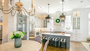Une cuisine moderne avec des meubles blancs, un îlot central doté de tabourets et des luminaires suspendus.