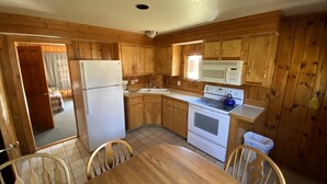 Une cuisine compacte avec des meubles en bois, un réfrigérateur blanc, une cuisinière et un four à micro-ondes. On y trouve également une table à manger avec des chaises.