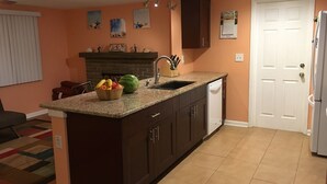 Uma cozinha com armários escuros, bancada de granito, máquina de lavar louça branca e uma fruteira.