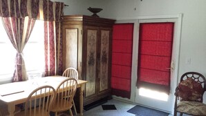 A dining area with a wooden table and chairs, a cabinet, and a door with red curtains. - Cozy Apartment on Cape Cod MA (Mashpee)