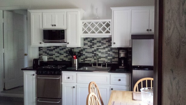 A compact kitchen with white cabinets, a microwave, a stove, and a sink. - Cozy Apartment on Cape Cod MA (Mashpee)