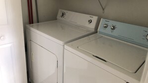 A laundry area with two white washing machines and a shelf above them. - Cozy Apartment on Cape Cod MA (Mashpee)