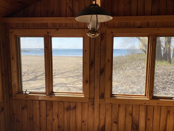 A room with wooden walls and three windows overlooking a beach.