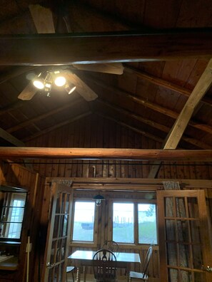 Cozy space with a high ceiling and exposed beams, featuring a table and chairs, a ceiling fan, and a window with an outdoor view.