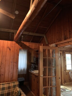 Cozy cabin interior with a high ceiling, plaid sofa, and kitchenette featuring a coffee maker and sink.