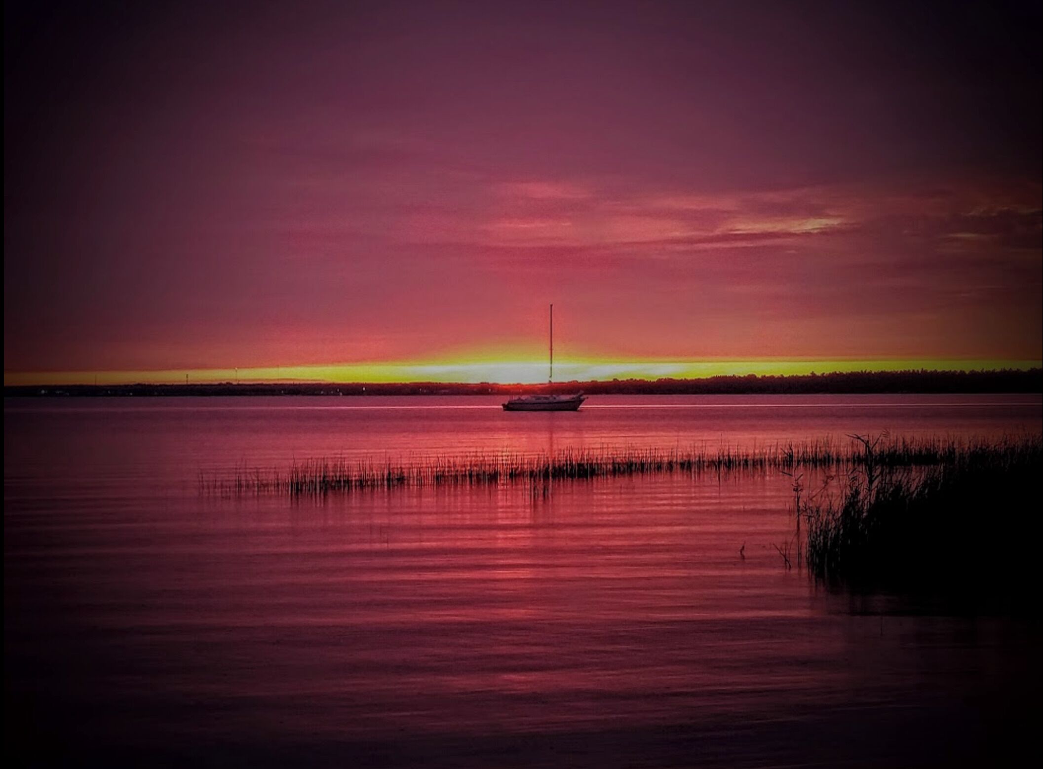 A calm body of water with a single boat anchored in the center, surrounded by a calm water surface reflecting the sky.
