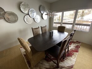 A dining area with a dark wooden table, beige upholstered chairs, and a patterned rug.