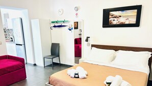 Une chambre d’hôtel avec un lit, une chaise, un canapé rouge, une horloge murale et un tableau encadré.