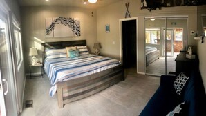 A bedroom with a bed, a nightstand, a lamp, a wall art piece, and a sliding door leading to another room. - The Beachfront Villa 13 (Earp)