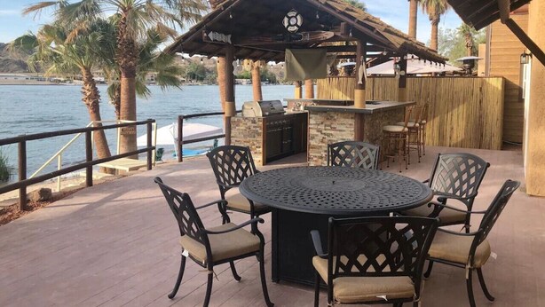 An outdoor patio with a round table and chairs, a grill, and a view of the water. - The Beachfront Villa 13 (Earp)