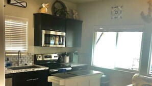 A compact kitchen with dark cabinets, a white island, and a dining area with a wooden table. - The Beachfront Villa 13 (Earp)