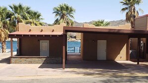 A building with a covered patio area, a pool in the background, and palm trees. - The Beachfront Villa 13 (Earp)