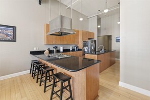 Uma cozinha moderna com ilha central, armários de madeira, eletrodomésticos de aço inoxidável e banquetas para bar.