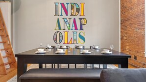 Taula de menjador preparada amb plats, bols i gots blancs, i una obra d'art colorida penjada al mur.