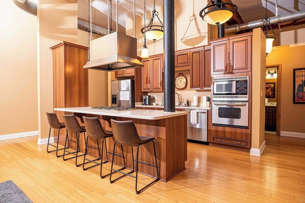 A kitchen with wooden cabinets, a central island with bar stools, stainless steel appliances, and pendant lighting.