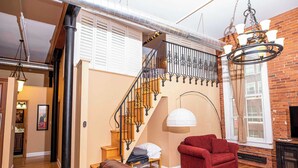 A living room with a brown leather sofa, a red armchair, a staircase with black railings, and a chandelier.