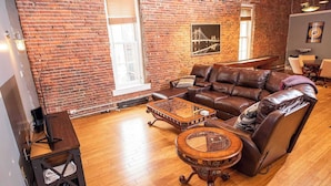 A living room with a brick wall, leather sofa, wooden coffee table, and a small side table.