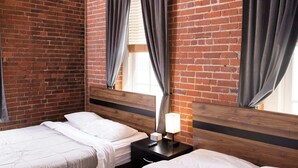 A room with two beds, a wooden headboard, a ceiling fan, and a brick wall.