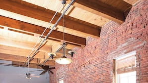 A dining area with a long wooden table, black chairs, a brick wall, and a ceiling fan.