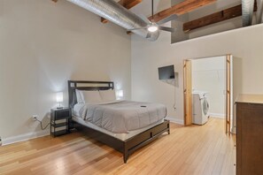 A bedroom with a bed, a nightstand, a ceiling fan, a washing machine, and a wooden wardrobe. - Top Floor Loft in Downtown Indianapolis!!! (Indianapolis)