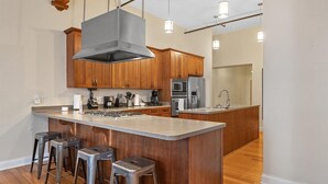 A modern kitchen with wooden cabinets, a central island with stools, stainless steel appliances, and pendant lighting. - Top Floor Loft in Downtown Indianapolis!!! (Indianapolis)