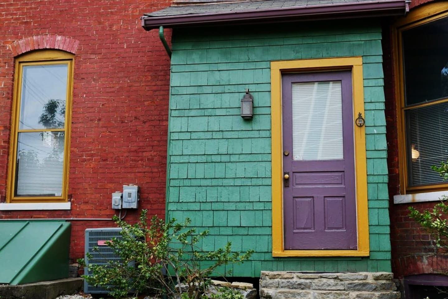 Une maison en briques rouges, avec une façade verte et une porte violette.