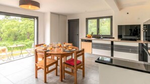 A modern kitchen with a central island, large windows, and a dining area with wooden chairs. - Apartment Paoli by Interhome (Porto Vecchio)