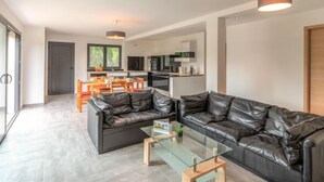 A modern living room with a glass coffee table, black leather sofas, and a kitchen in the background. - Apartment Paoli by Interhome (Porto Vecchio)