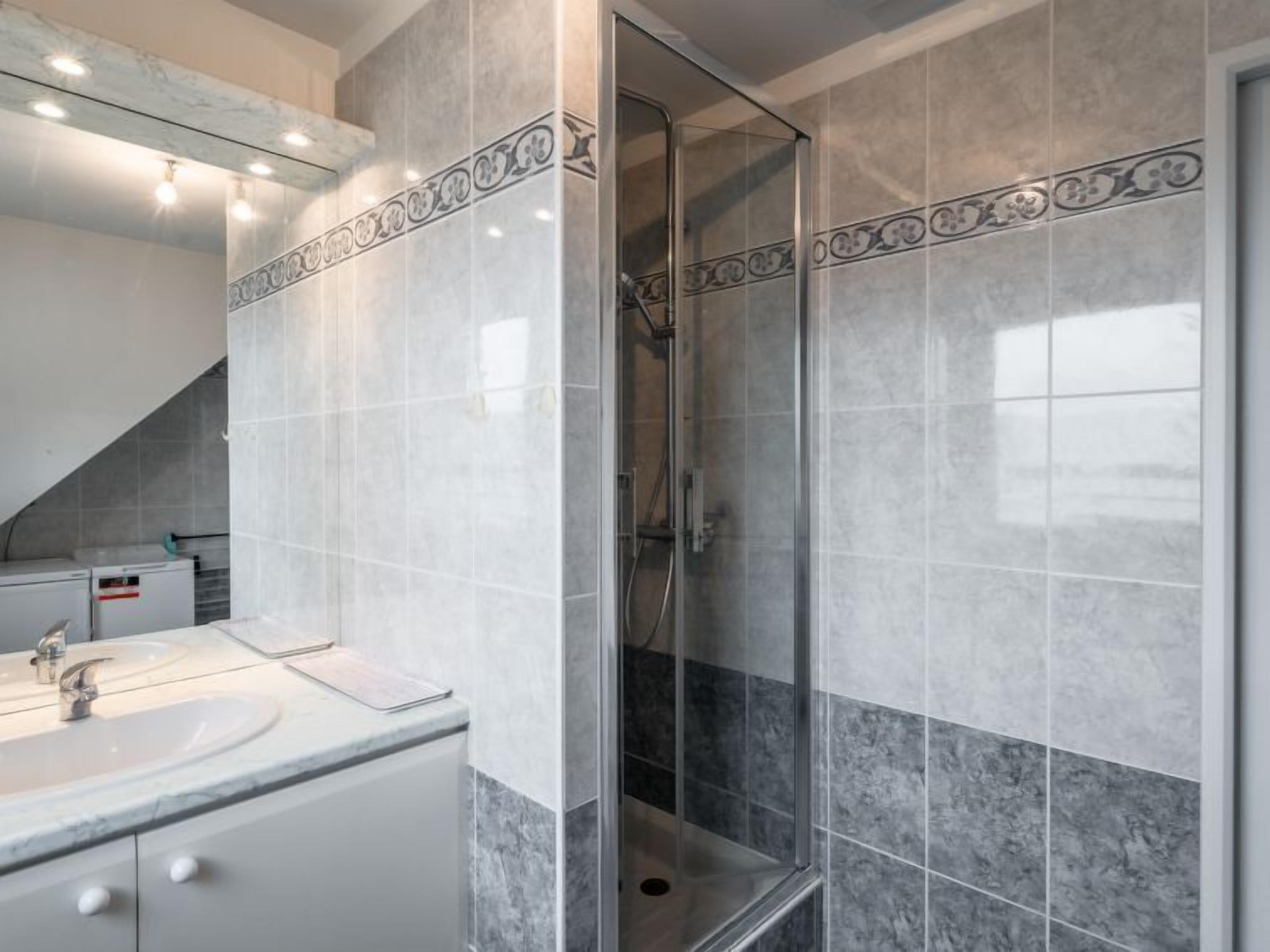 Uma casa de banho moderna com cabine de duche em vidro, toucador com lavatório e detalhes em mosaico decorativo.