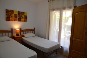 Quarto com duas camas de solteiro, mesa de cabeceira com abajur, guarda-roupa de madeira e janela com cortinas leves.