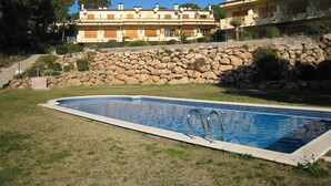 Una piscina con un muro de piedra y un edificio con varios balcones al fondo.