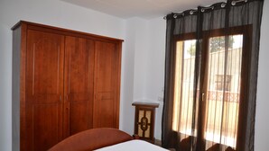 Un dormitorio con un armario de madera, una mesita de noche y una ventana con cortinas.