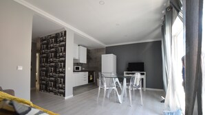 Ein modernes Wohnzimmer mit einer Couch, einem Glastisch mit Stühlen, einer Küchenzeile inklusive Mikrowelle und einem Fernseher.