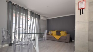 Ein modernes Wohnzimmer mit einem Glastisch, klaren Stühlen, einer gelben Kissensofa und einer grauen Wand.