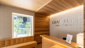 Un espace d’accueil comprenant un banc en bois, un comptoir de réception et un mur sur lequel est inscrit le texte « GRAND BASE FUKUOKA TENJIN ».