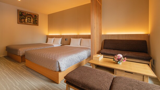 Une chambre d’hôtel avec deux lits, un canapé, une petite table ornée d’un vase de fleurs et un tableau accroché au mur.