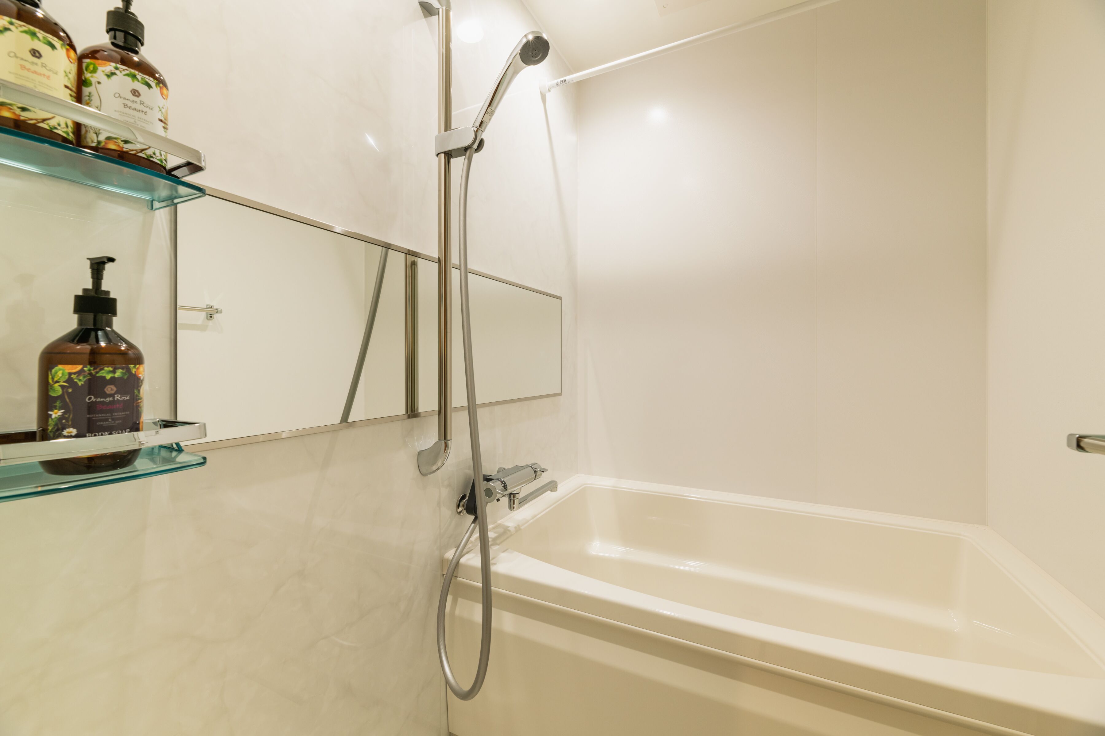 A bathroom with a bathtub, a glass shelf with toiletries, and a mirror.
