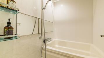 A bathroom with a bathtub, a glass shelf with toiletries, and a mirror.