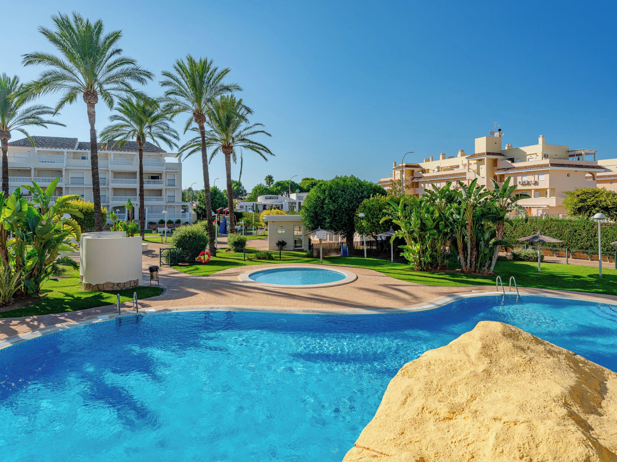 A resort with a swimming pool, palm trees, and a building with multiple balconies.