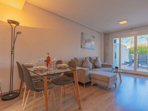 Un salon moderne avec une table à manger en verre, un canapé gris recouvert de tissu et un tableau accroché au mur.