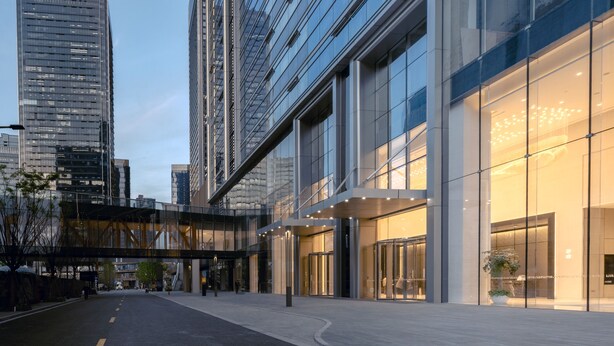 Un hotel moderno con fachada de vidrio, entrada cubierta y vistas de edificios altos circundantes.