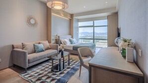 Una habitación de hotel moderna con sofá, cama, escritorio y un ventanal que ofrece vistas a la ciudad.